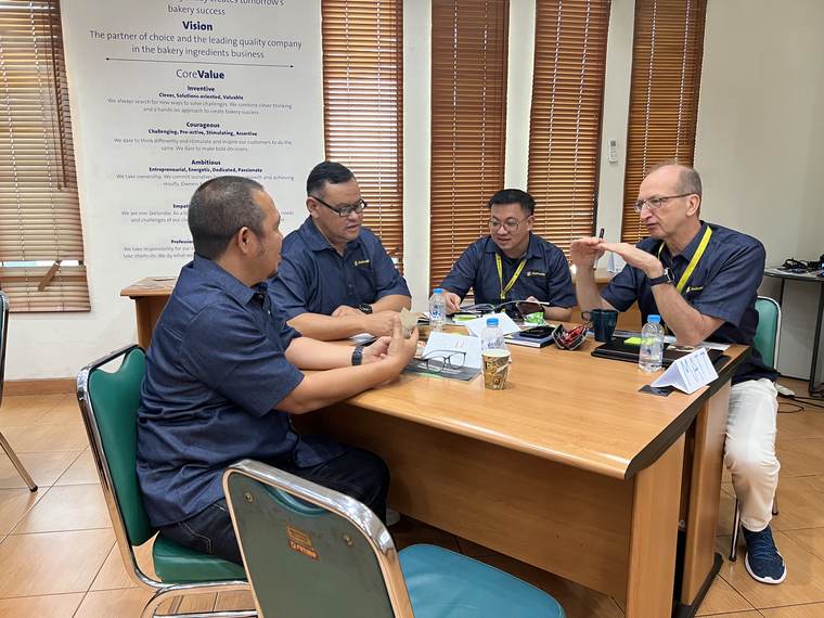 Empat peserta berdiskusi mengelilingi meja kayu di ruang rapat.